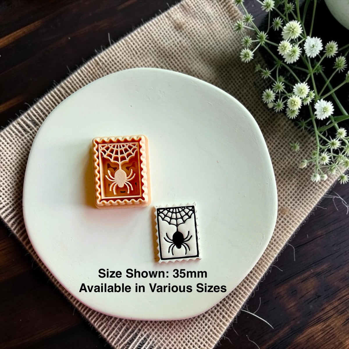 Matching spider web polymer clay cutter beside the finished clay design with 35mm size reference on a white dish.