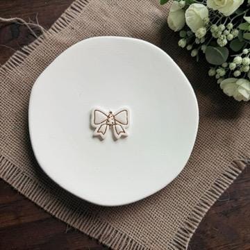 Finished white polymer clay Christmas bow with a tiny tree detail, displayed on a white plate.
