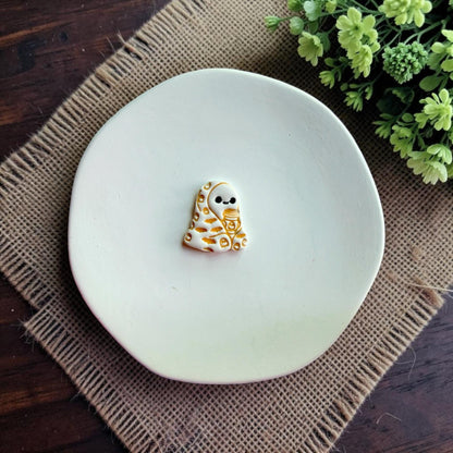 Finished polymer clay ghost wrapped in a blanket holding a coffee cup displayed on a white dish.