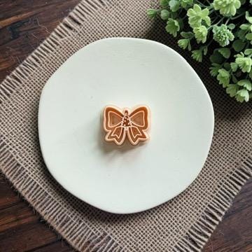 Christmas bow polymer clay cutter featuring a small Christmas tree in the center, displayed on a white plate.