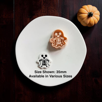 Polymer clay cutter and finished skeleton ghost clay piece displayed together on a white round surface with a pumpkin in the background.