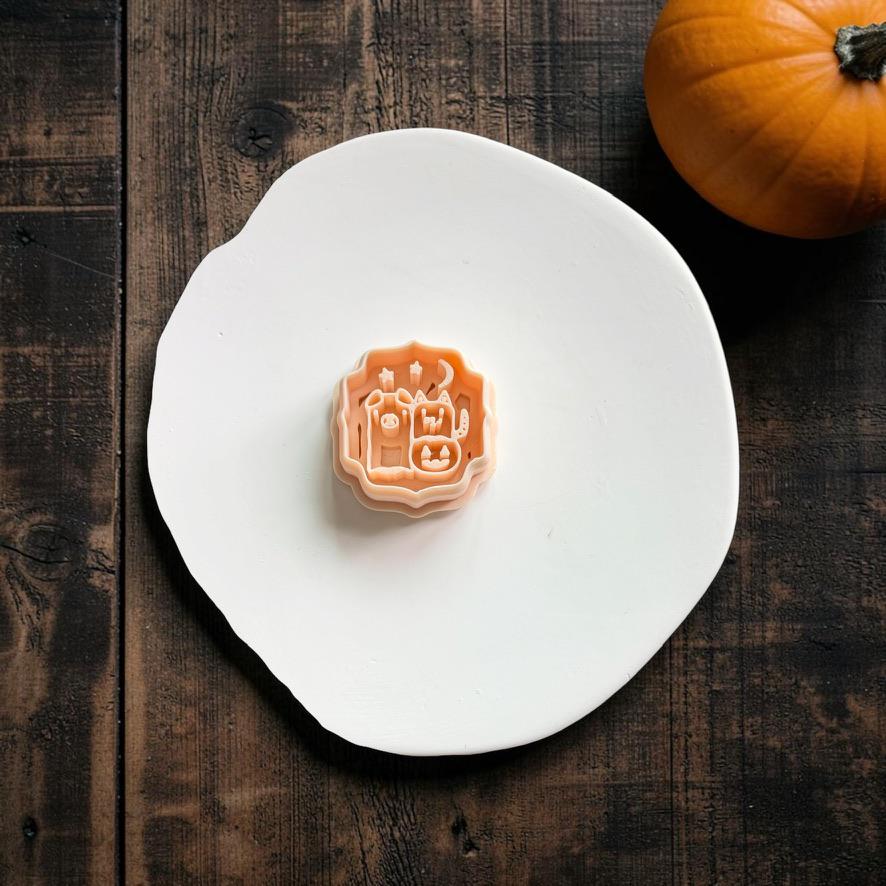 Peach Halloween Pals polymer clay cutter centered on a white clay slab, featuring two costumed characters, a jack-o-lantern treat basket, crescent moon, and stars, with an orange pumpkin in the upper right.