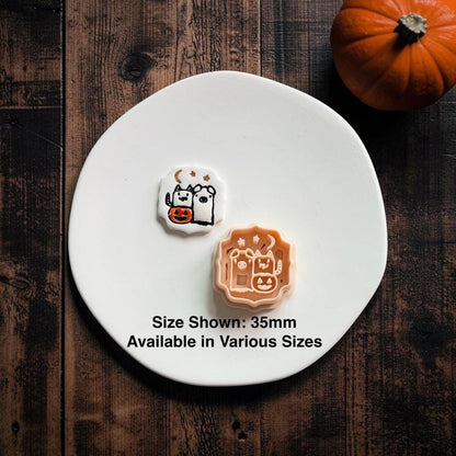 Finished Halloween Pals clay piece beside the peach design on a white clay slab, showing the ghost and cat characters, jack-o-lantern basket, moon, and stars; text notes the size shown is 35mm and various sizes are available.