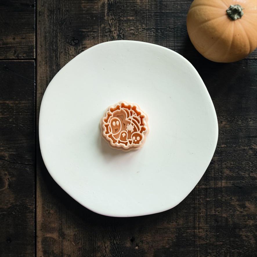 Orange-and-white spooky polymer clay cutter centered on a white plate against a dark wood background with a pumpkin nearby.