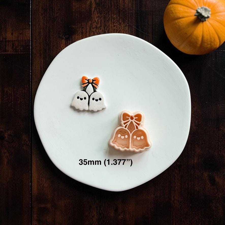 Finished white and orange ghost cherries piece displayed beside the matching peach design on a white plate, with an orange pumpkin in the upper right.