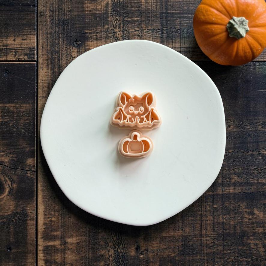 Peach bat and separate pumpkin designs displayed vertically on a large white plate with the bat above the pumpkin and an orange pumpkin in the upper right background.