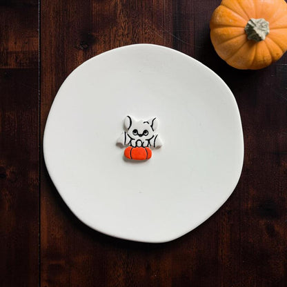 Finished clay example centered on a white plate showing a white bat with black details perched over a bright orange pumpkin.