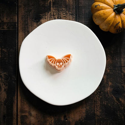 Peach-colored Skull Bat polymer clay cutter centered on a white plate, showing the skull face and detailed bat wing impression lines.