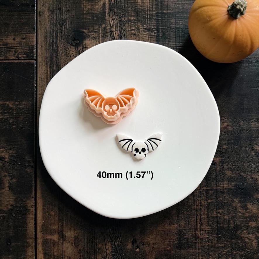 Skull Bat cutter displayed above the finished white and black clay example on a white plate with a pumpkin in the background.