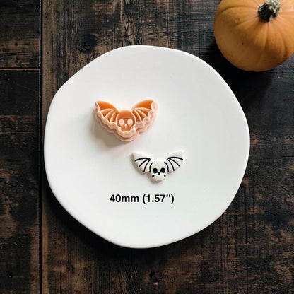 Skull Bat cutter displayed above the finished white and black clay example on a white plate with a pumpkin in the background.