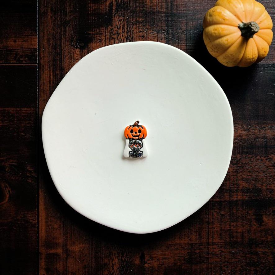 Finished Pumpkin Ghost with Kitty clay piece centered on a white plate, featuring an orange jack-o-lantern pumpkin head and small dark kitty.