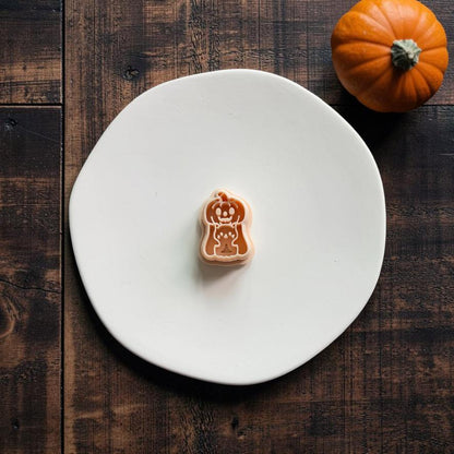 Peach-colored Pumpkin Ghost with Kitty polymer clay cutter centered on a white plate with an orange pumpkin in the upper right.