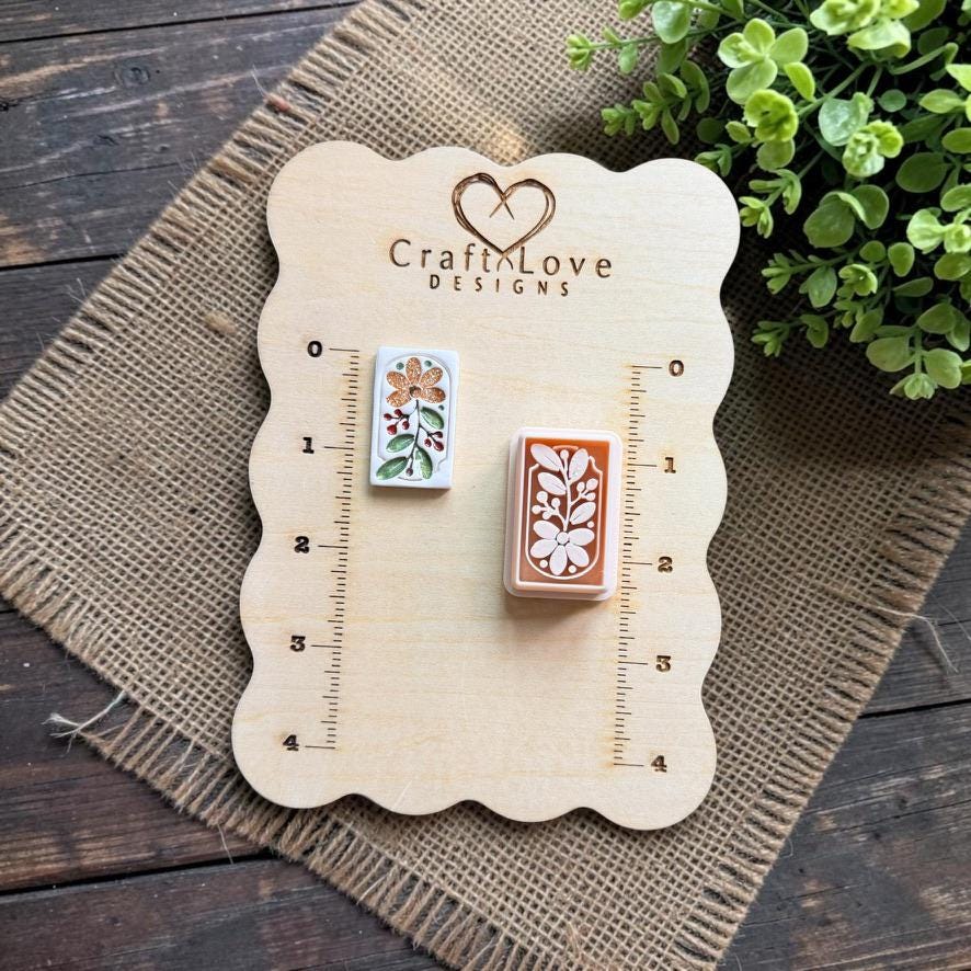 Finished floral clay piece and matching rectangular botanical cutter displayed on a wooden measuring board, showing the relative size and detailed flower and leaf pattern.