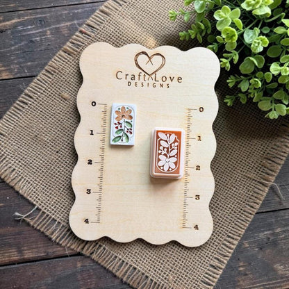 Finished floral clay piece and matching rectangular botanical cutter displayed on a wooden measuring board, showing the relative size and detailed flower and leaf pattern.