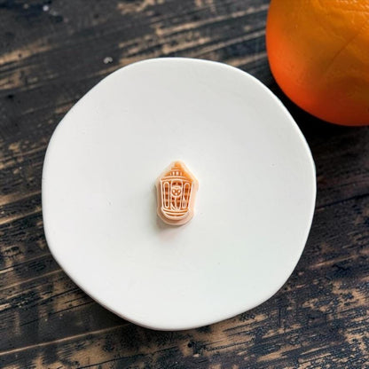 Peach Halloween lantern polymer clay cutter centered on a white plate with a pumpkin in the background.