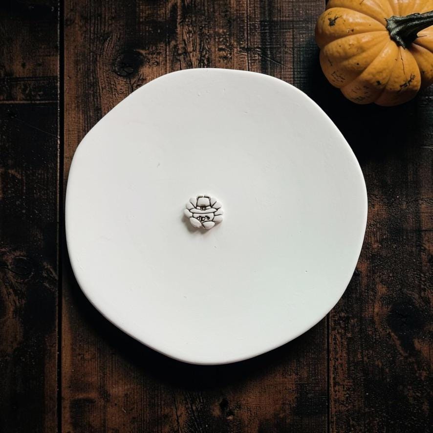 Finished white miniature turkey clay piece with dark outlined details displayed on a white plate beside a fall pumpkin.