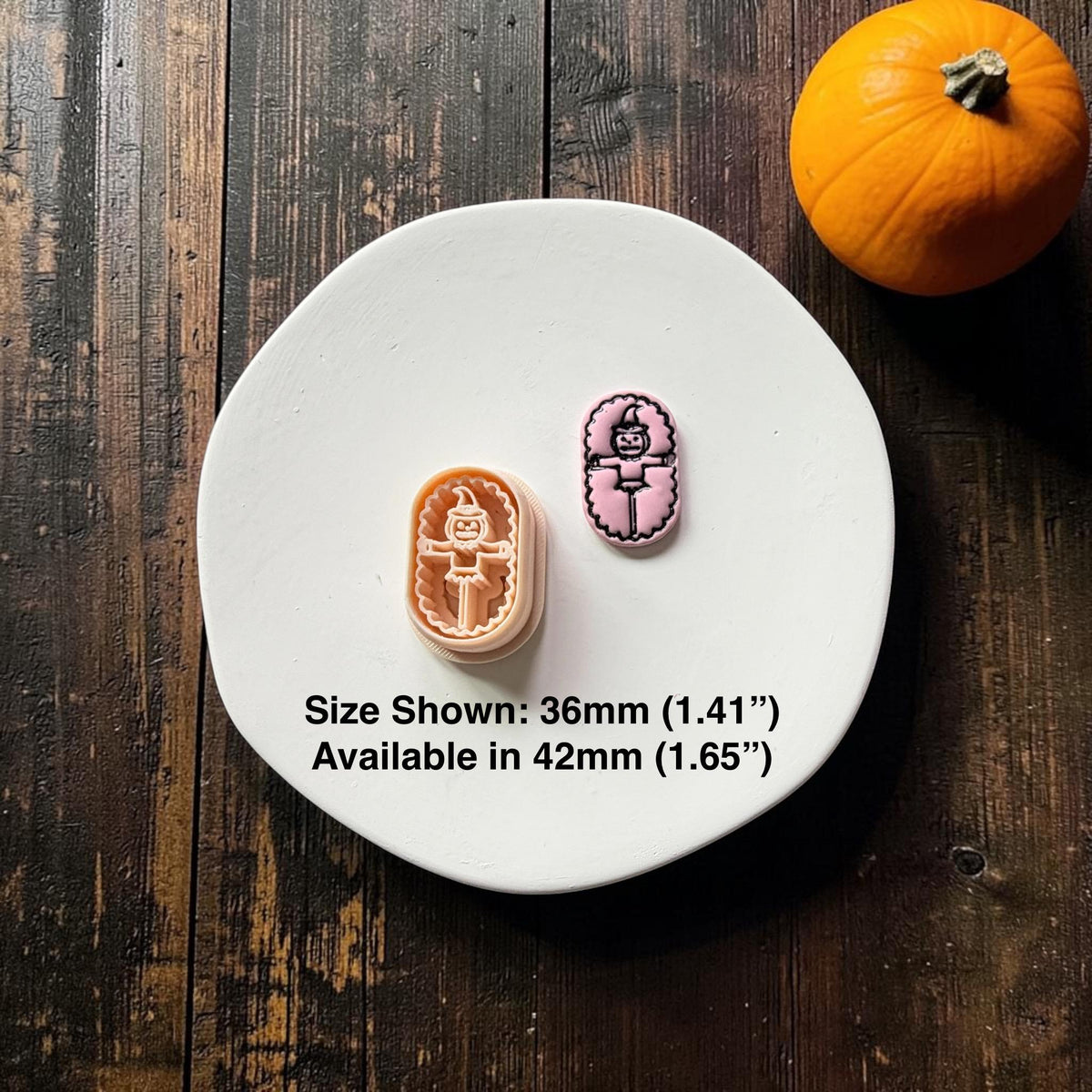 Orange pumpkin scarecrow polymer clay cutter beside a finished pink clay example with black detailing, displayed on a white round surface with a pumpkin in the background.