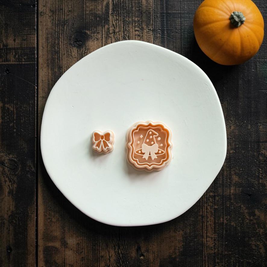 Peach witch hat design and separate matching bow displayed together on a large white clay slab with an orange pumpkin in the background.