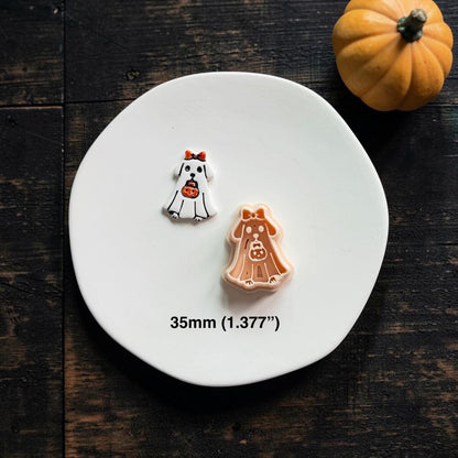 Finished white ghost-costume puppy piece displayed beside the matching peach design on a white plate, with a small orange pumpkin in the upper right.