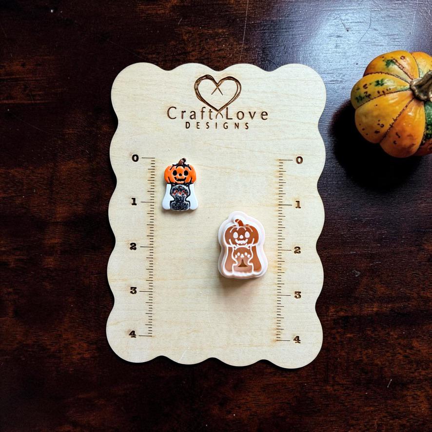 Finished Pumpkin Ghost with Kitty clay piece and matching peach-colored cutter displayed on a wooden measuring board to show relative size and design detail.