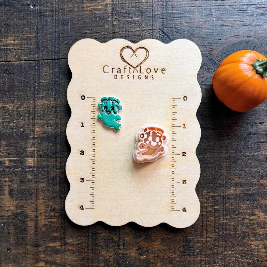 Green finished FrankenGhost polymer clay piece beside the matching peach-colored cutter on a wooden Craft Love Designs measuring board with a pumpkin nearby.