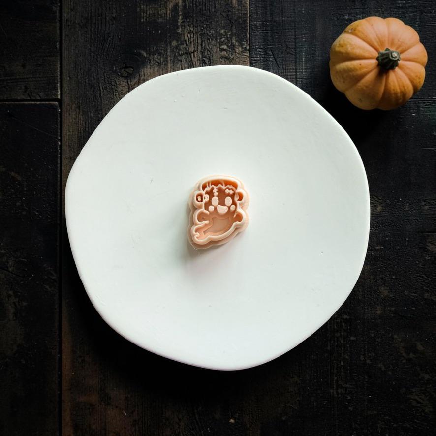 Peach-colored FrankenGhost polymer clay cutter centered on a white plate, showing the Frankenstein-inspired face, stitches, and flowing ghost shape.
