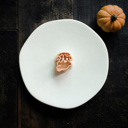 Peach-colored FrankenGhost polymer clay cutter centered on a white plate, showing the Frankenstein-inspired face, stitches, and flowing ghost shape.
