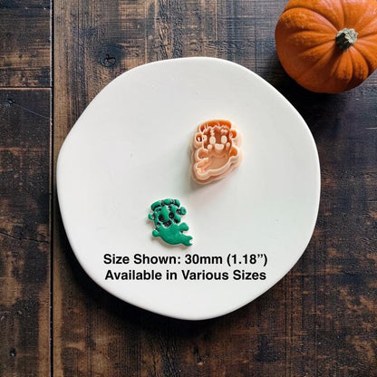 FrankenGhost cutter displayed above a finished green and black clay example on a white plate with an orange pumpkin in the background.