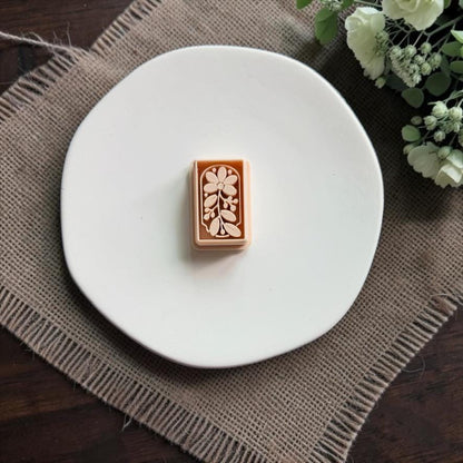Peach rectangular polymer clay cutter centered on a white plate, featuring an embossed flower, leafy branch, and small botanical details.