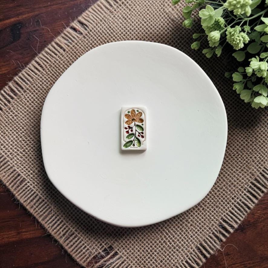 Finished white rectangular clay piece decorated with a glittery gold flower, green leaves, and deep red berry accents on a white plate.