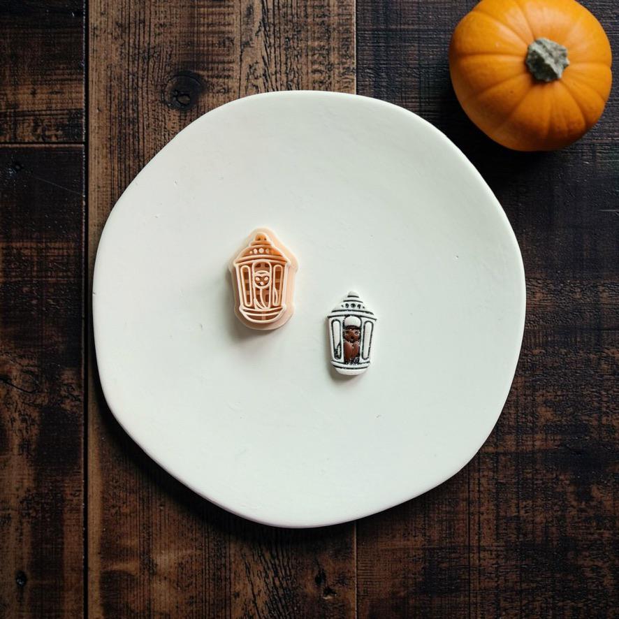 Matching bat lantern polymer clay cutter and finished decorated clay example displayed together on a white plate with an orange pumpkin in the background.