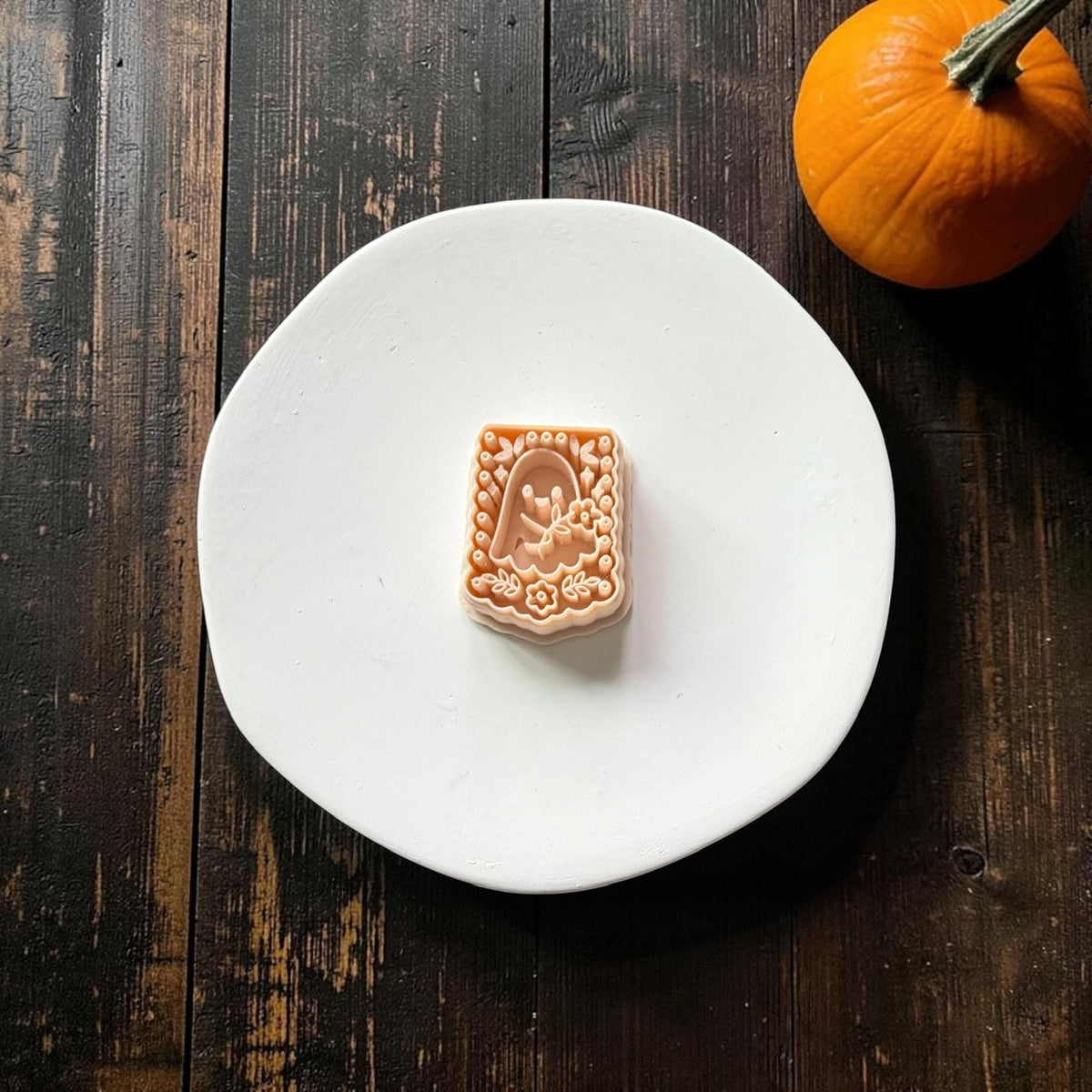 Peach rectangular clay design centered on a white plate, featuring a cute ghost holding flowers surrounded by blossoms, leaves, bats, stars, and a decorative dotted border.