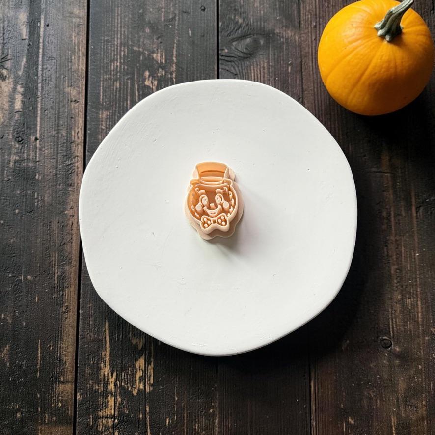 Peach-colored design featuring a smiling vintage crescent moon face wearing a top hat and bow tie, centered on a white round surface with an orange pumpkin in the upper right.