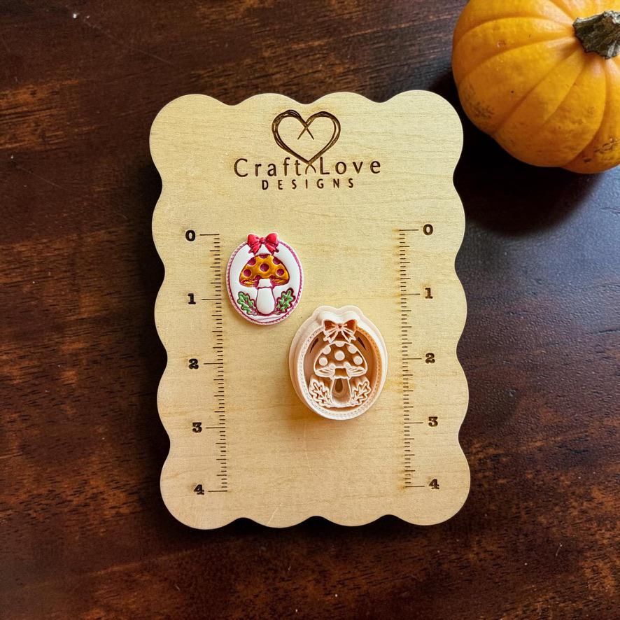 Finished colorful mushroom piece and matching peach-colored design displayed on a Craft Love Designs wooden measuring bo