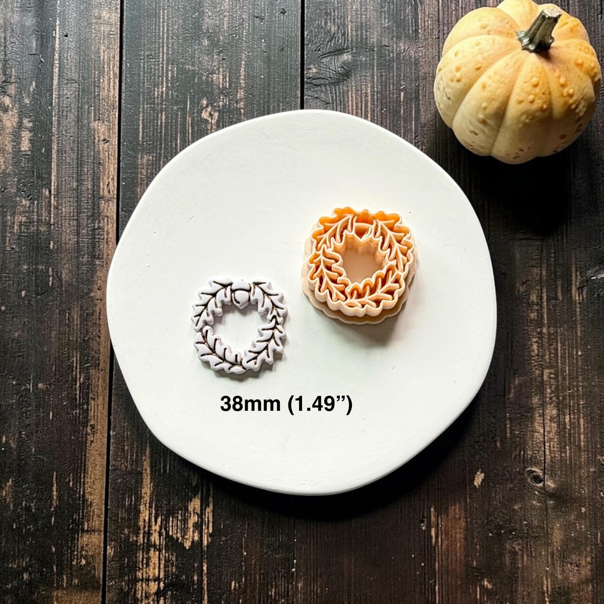Finished white oak leaf and acorn wreath beside the orange polymer clay cutter on a white round surface, with text showing the 38mm (1.49") size.