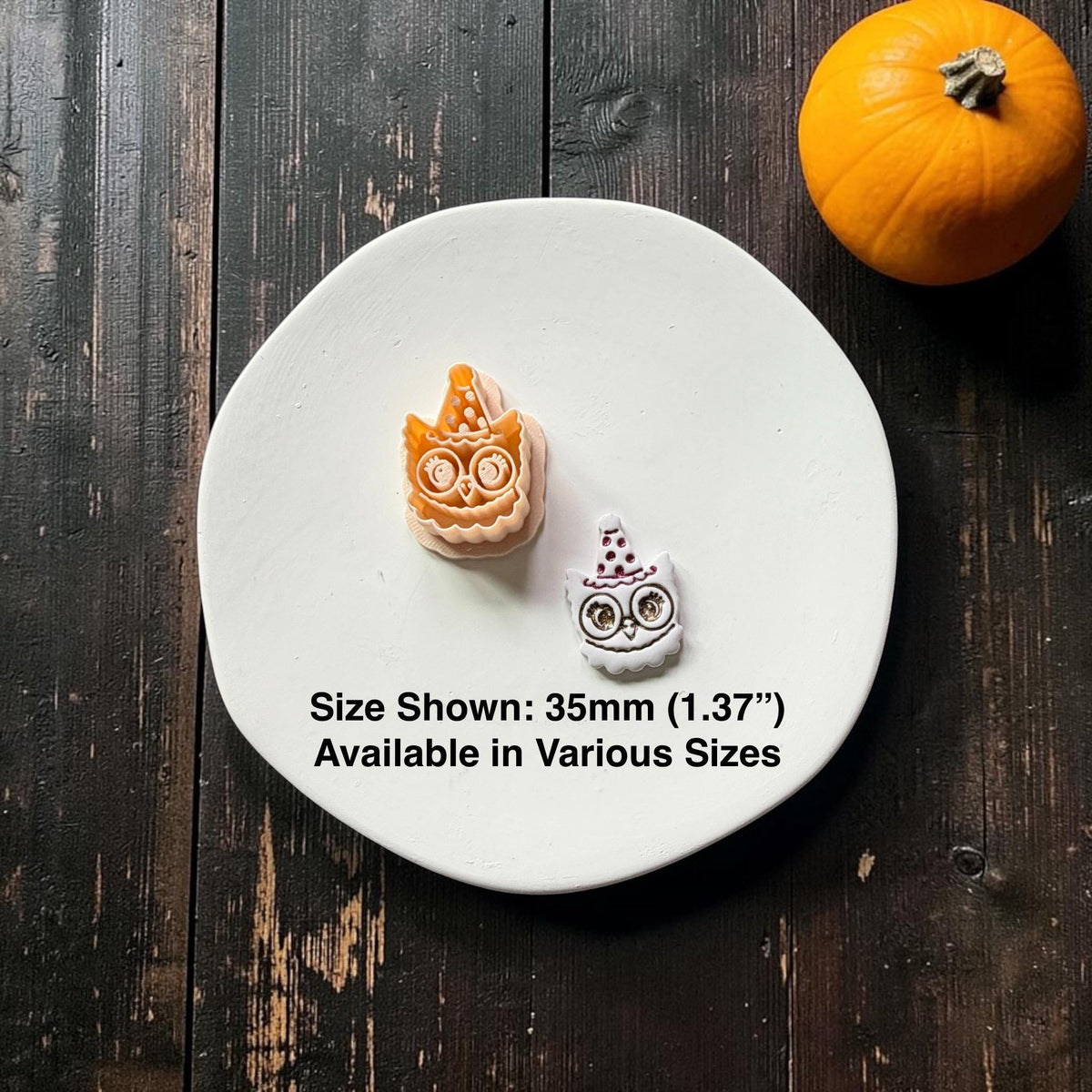 Orange owl design beside a finished white version, both featuring oversized round eyes, scalloped feathers, and pointed witch hats; text states size shown 35mm (1.37") and available in various sizes.