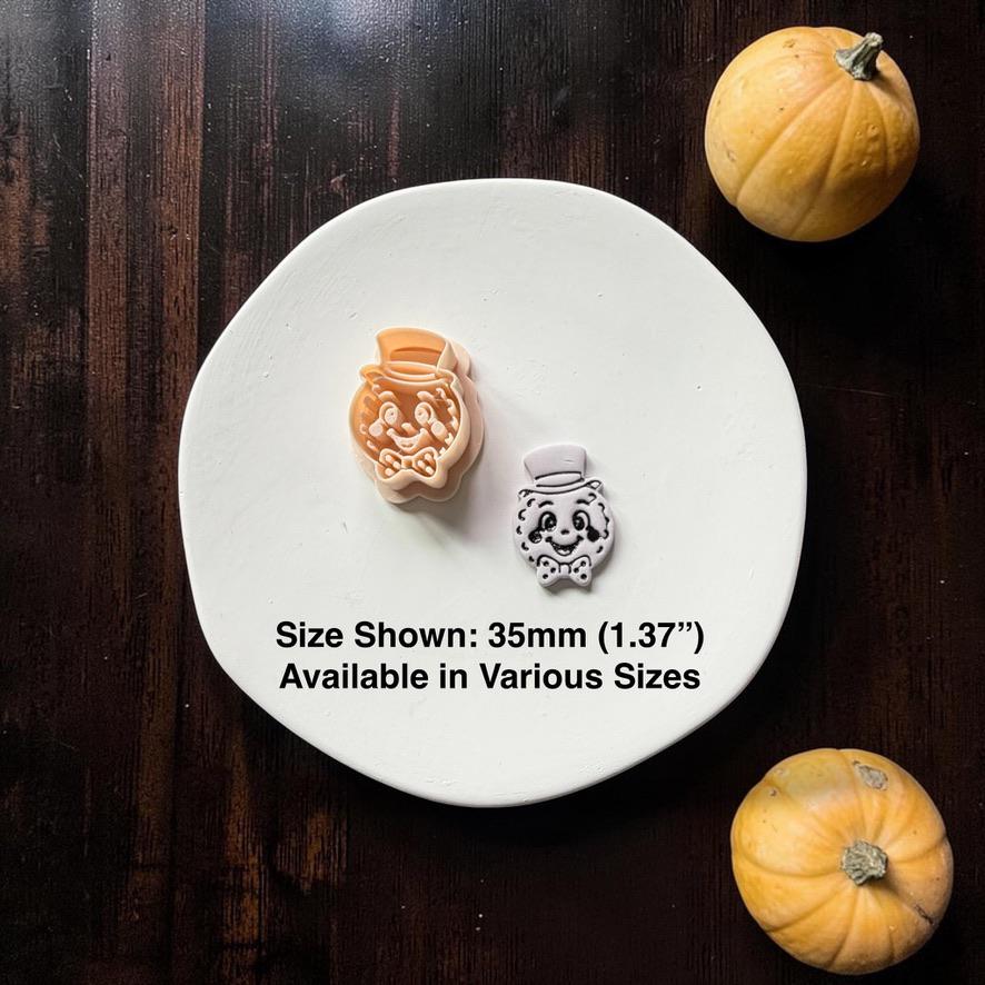 Peach-colored design beside a finished white smiling moon face with top hat and bow tie on a white round surface, surrounded by two small pumpkins; text states size shown 35mm (1.37") and available in various sizes.