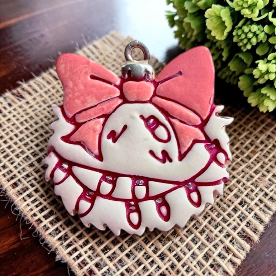 Close-up of the finished pink and white Christmas ornament featuring a large pink bow, shaggy outer edge, and strand of dangling holiday lights, with a silver ornament loop at the top.