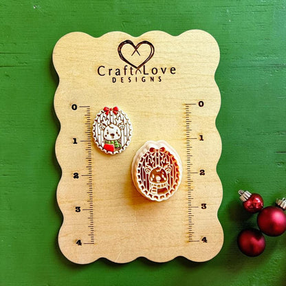Finished Christmas reindeer design and matching clay cutter displayed on a Craft Love Designs wooden measurement board against a green background, with red Christmas ornaments at the lower right.