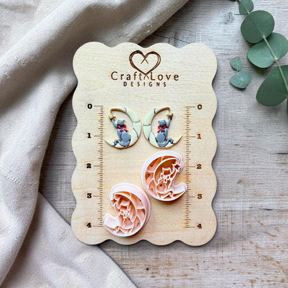 Two finished mirrored gray cat and crescent moon pieces displayed above their two matching separate designs on a Craft Love Designs wooden measurement board.