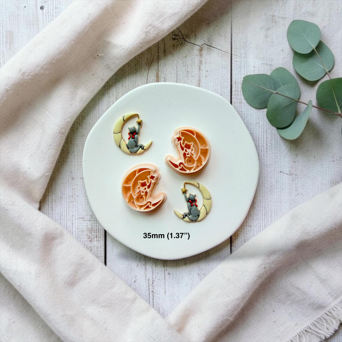 Mirrored cat and crescent moon designs shown with their finished clay examples on a white plate, with each cat facing the opposite direction and text showing the 35mm (1.37 inch) size.