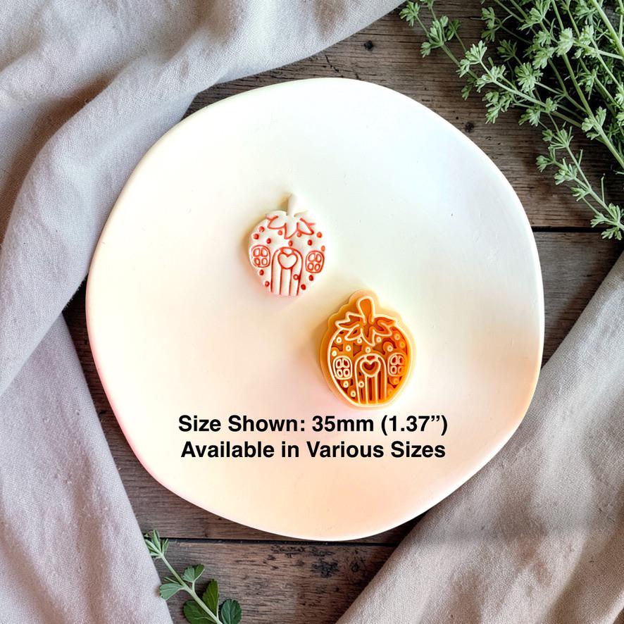 Finished white strawberry house clay piece displayed beside the orange design on a white plate, with text stating size shown is 35mm (1.37 inches) and various sizes are available.