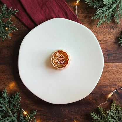 Orange hot cocoa design centered on a white plate, showing the scalloped round border and detailed mug with heart, whipped topping, botanical accents, and candy cane.
