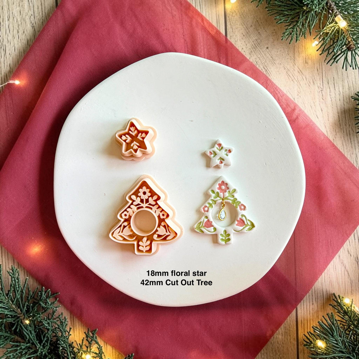Folk art Christmas tree cutter set shown beside the finished decorated earring. The example features a floral star topper, detailed white tree with pink and green folk flowers, and dangling teardrop charm. Text identifies the examples as an 18mm floral star and 42mm cutout tree.