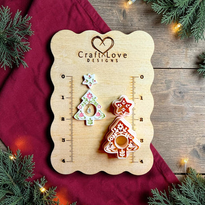 Two-part folk art Christmas tree polymer clay cutter set displayed beside a finished white Christmas tree earring with pink and green floral details. The design includes a floral star topper and decorative cutout tree with a hanging teardrop charm.
