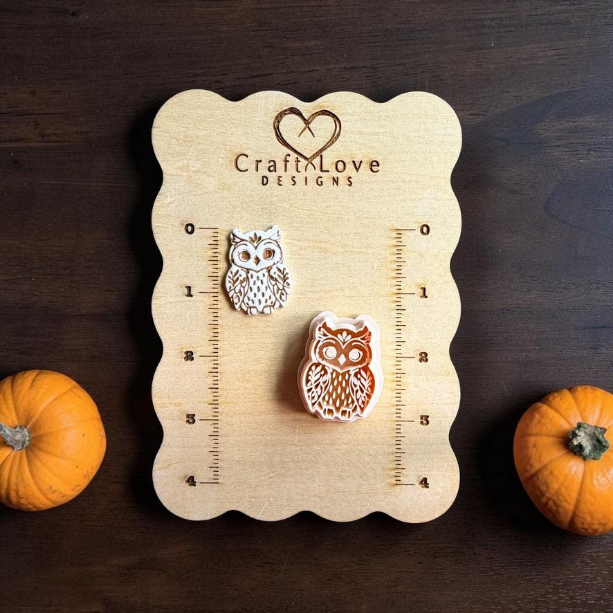 Finished white owl clay piece and matching owl polymer clay cutter displayed on a wooden Craft Love Designs sizing board, with small orange pumpkins on each side.