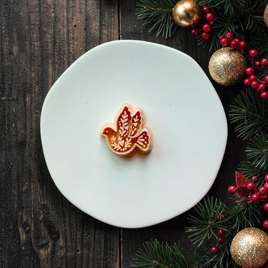 Peach-colored flying dove design centered on a white round surface, featuring leafy botanical patterns inside the wings and body, with Christmas greenery, red berries, and gold ornaments along the right side.