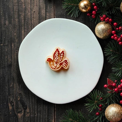 Peach-colored flying dove design centered on a white round surface, featuring leafy botanical patterns inside the wings and body, with Christmas greenery, red berries, and gold ornaments along the right side.