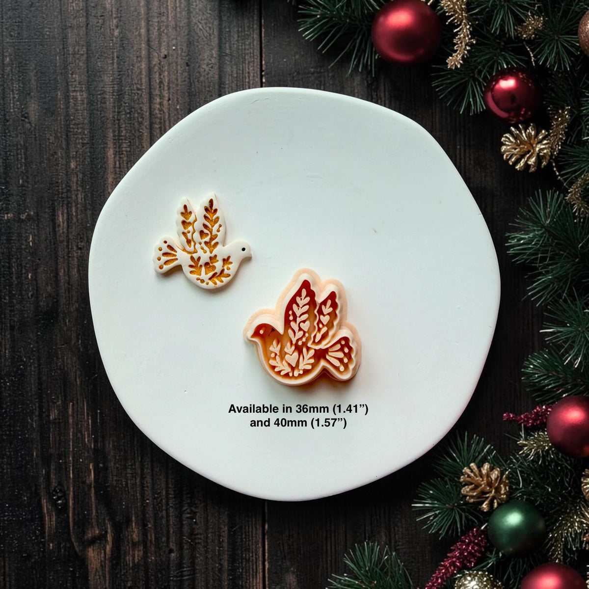 White and gold finished dove beside the larger peach-colored version on a white round surface decorated with Christmas greenery and ornaments. Text states the design is available in 36mm (1.41") and 40mm (1.57").