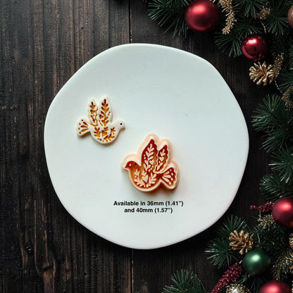White and gold finished dove beside the larger peach-colored version on a white round surface decorated with Christmas greenery and ornaments. Text states the design is available in 36mm (1.41") and 40mm (1.57").